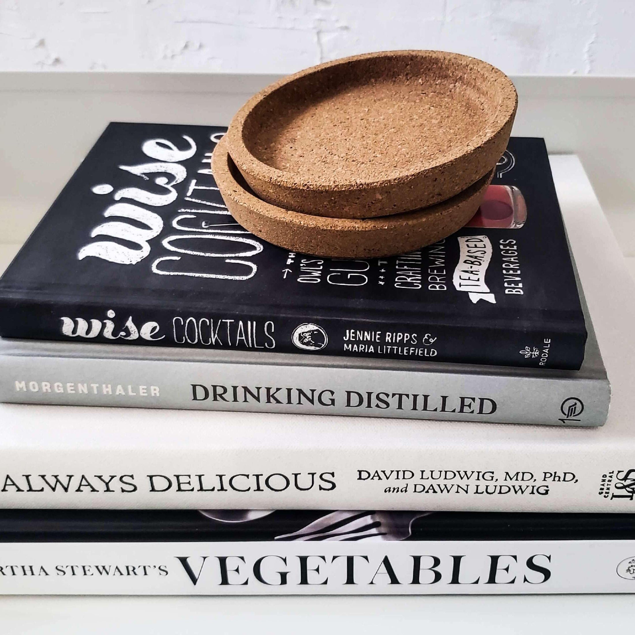 Stack of white and black cocktail books and cookbooks with ikea cork coasters on top. Real hardcover books staged and used for display. 