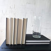 Hardcover books and glass vase staged for display. Stack of hardcover books in purplish gray and black.