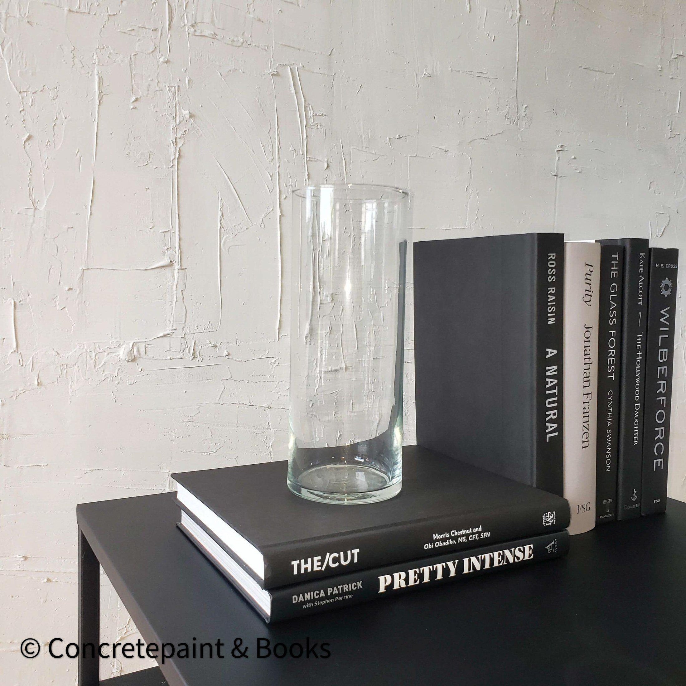 Hardcover books and glass vase staged for display. Stack of hardcover books in purplish gray and black.