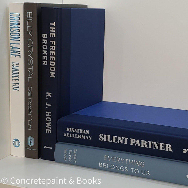 Stack of real hardcover books used as shelf décor in blues, white, and gray. Books on white ikea bookshelf.