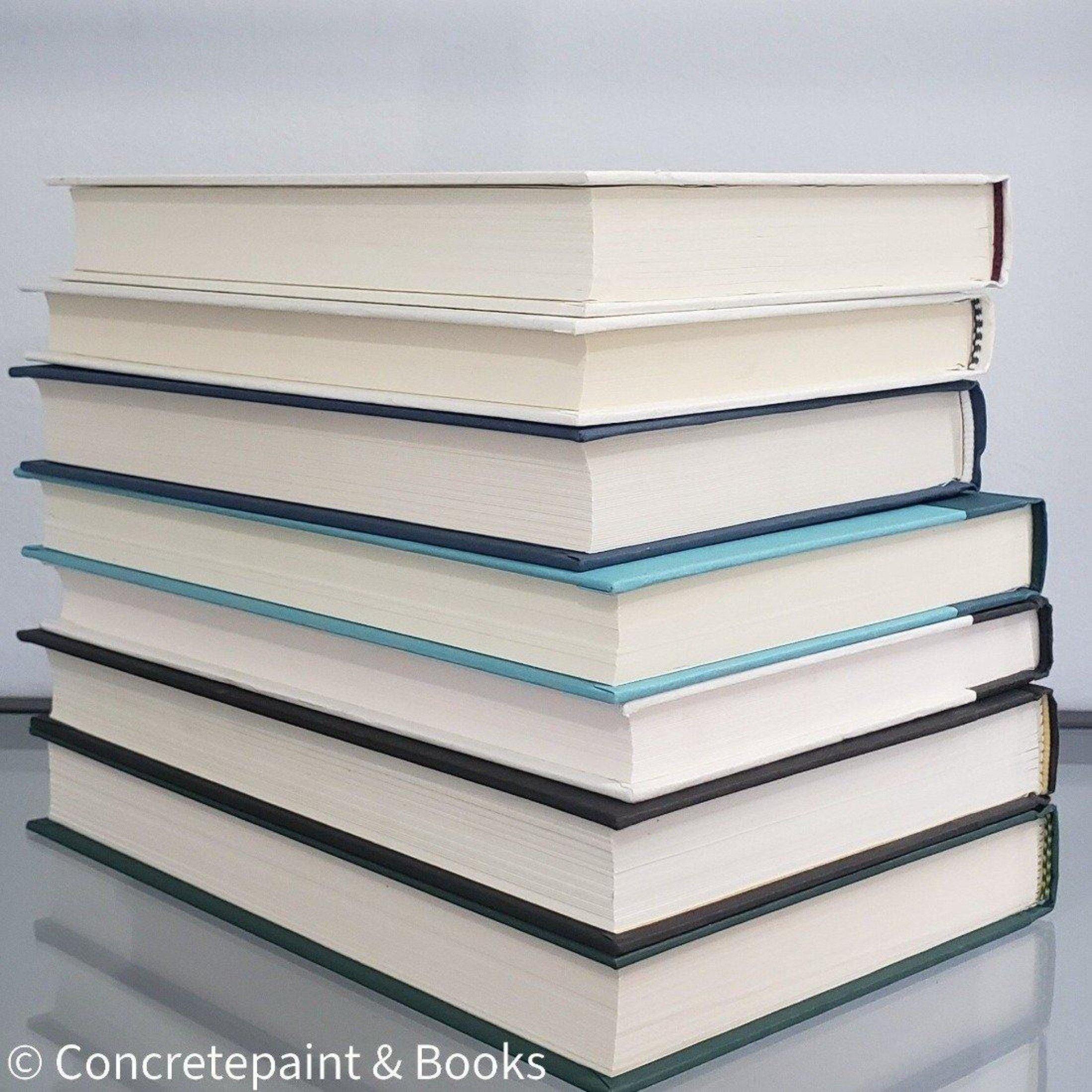 stack of 7 hardcover books on shelf display with green, blue, black and neutral binding.
