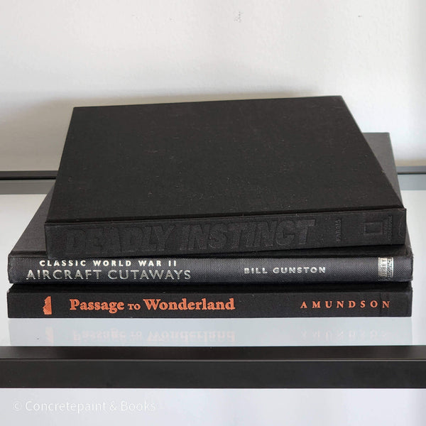 Stack of black rectangular coffee table books used as men's home décor. Aircraft, animals, and travel books.